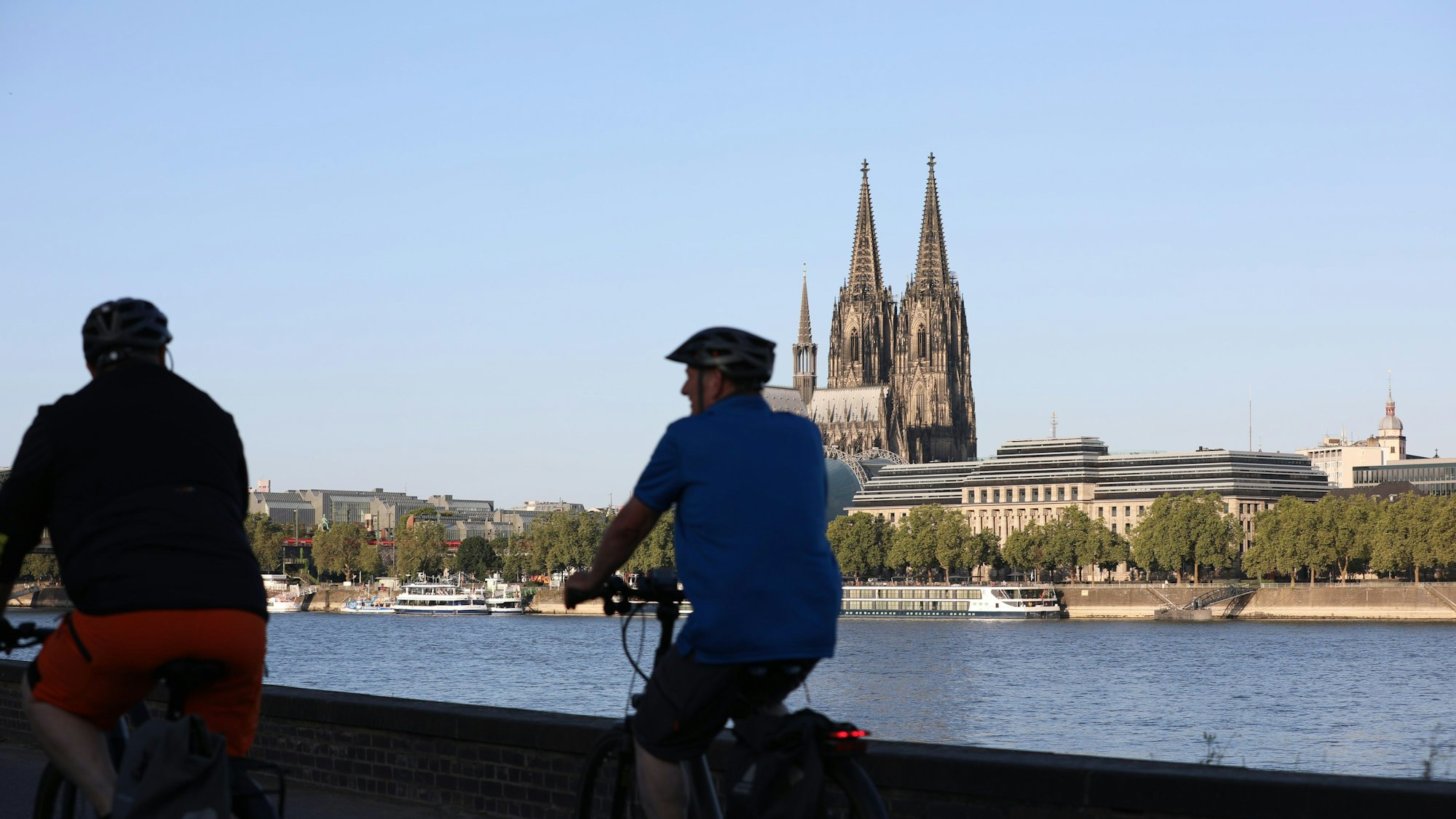 Radfahrer fahren am Rheinufer entlang, im Hintergrund ist der Kölner Dom zu sehen