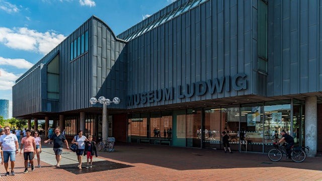 Zu sehen ist das Museum Ludwig in Köln in der Außenansicht. Davor befinden sich mehrere Menschen.