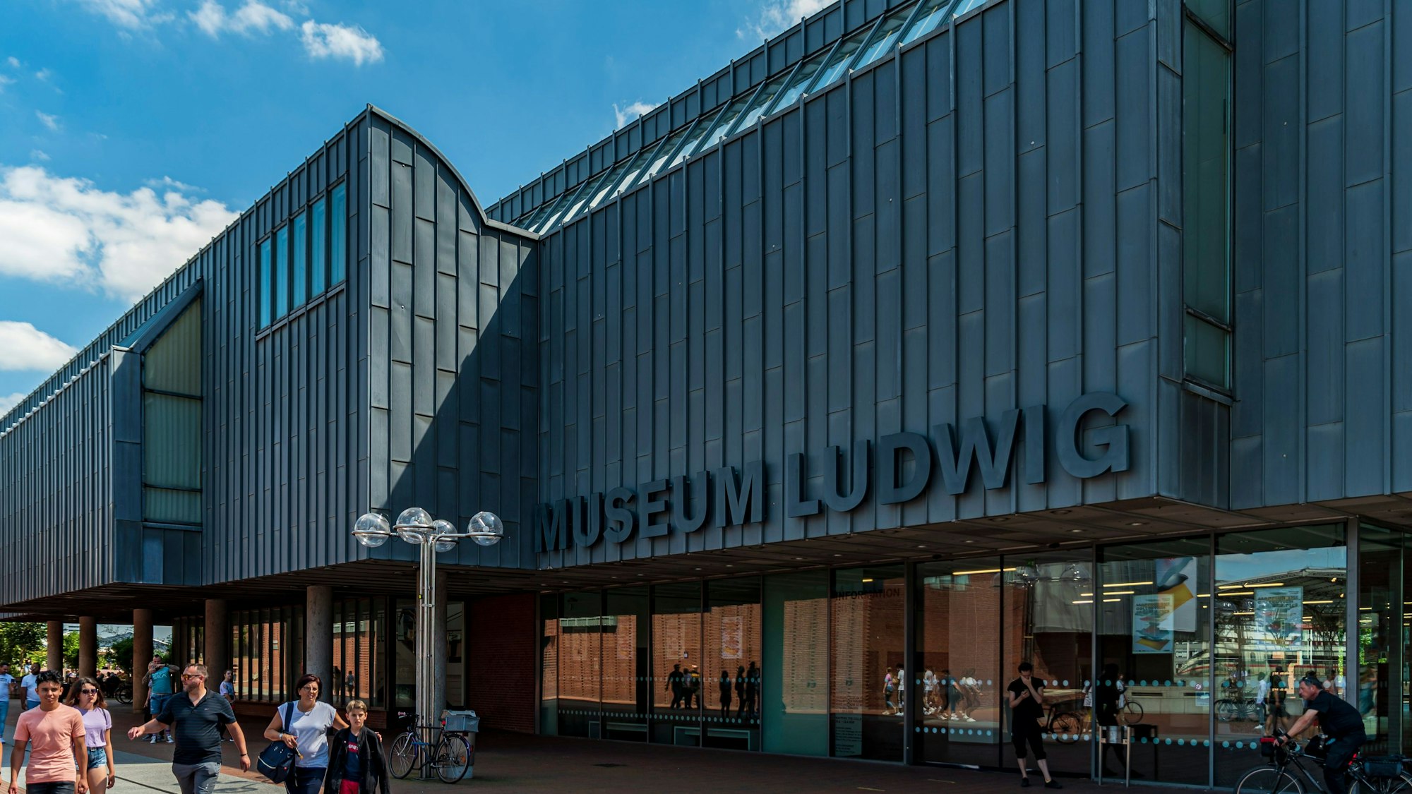 Zu sehen ist das Museum Ludwig in Köln in der Außenansicht. Davor befinden sich mehrere Menschen.