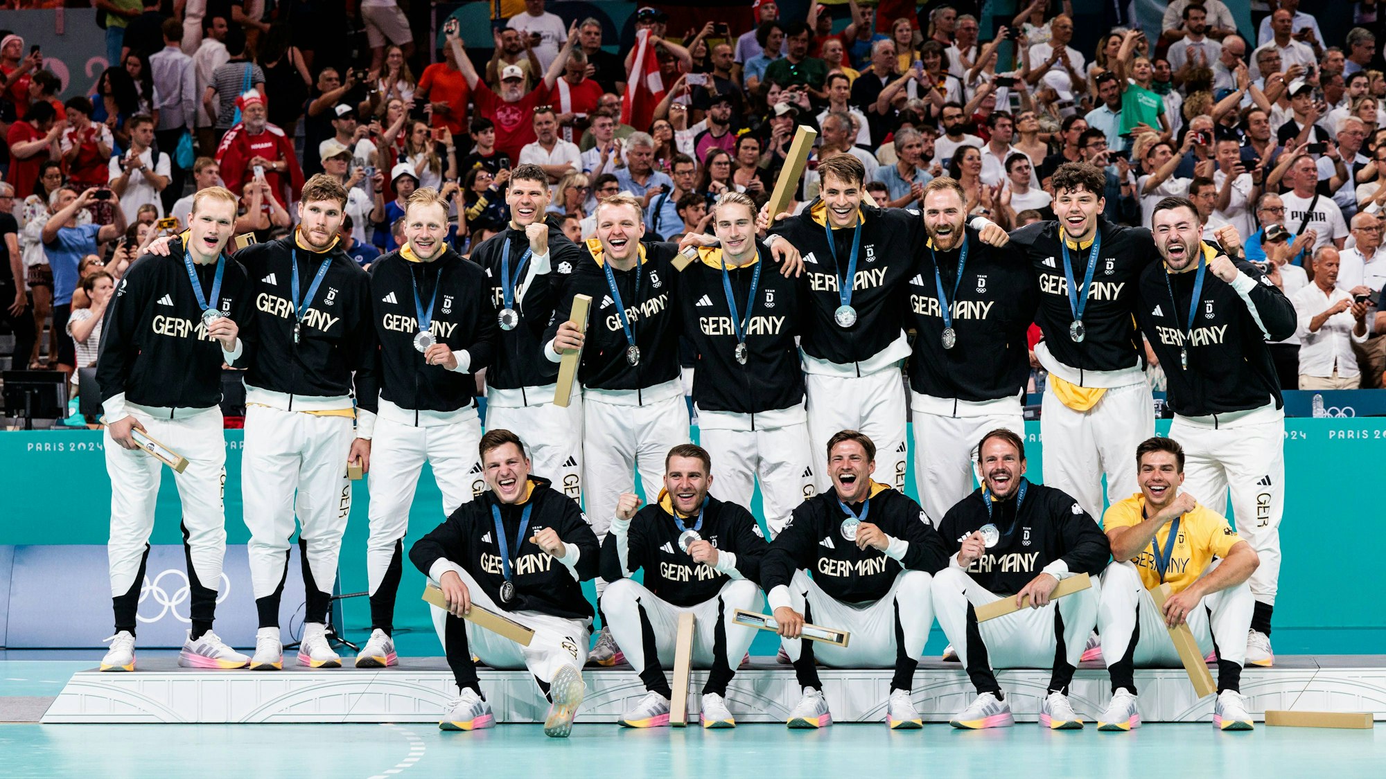 Die Männer der Handballnationalmannschaft stehen und sitzen mit Silbermedaillen auf dem Siegerpodest.