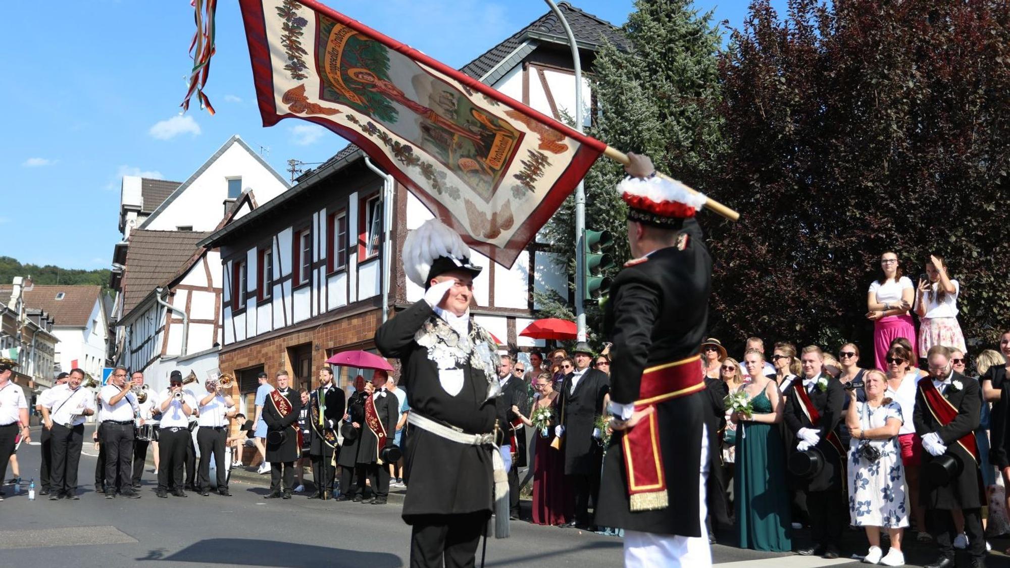 Ein Fahnenschwenker mit dem neuen König, am Straßenrand stehen viele Zuschauer.