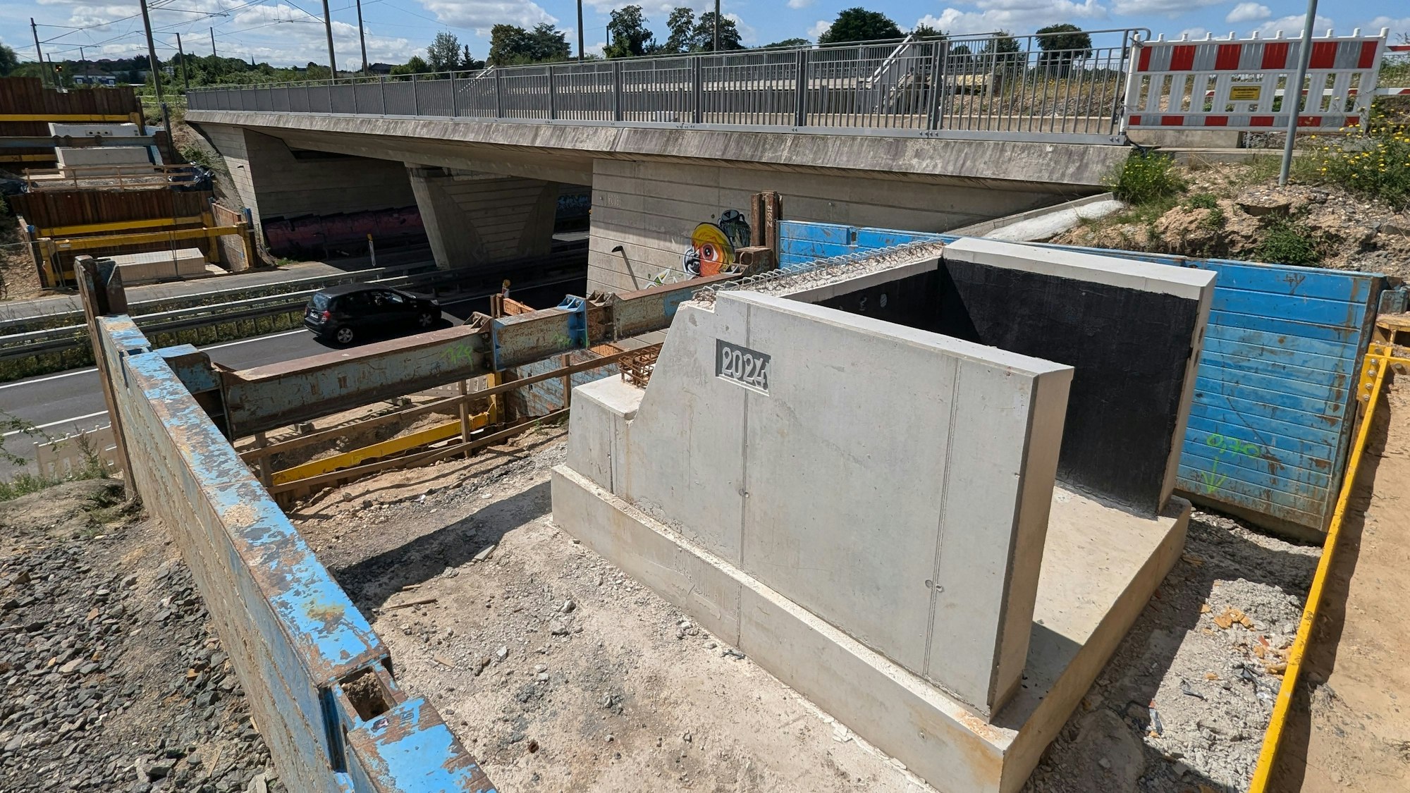 Ein Brückenfundament mit der eingegossenen Jahreszahl 2024 neben einer Brücke über eine vierspurige Straße.