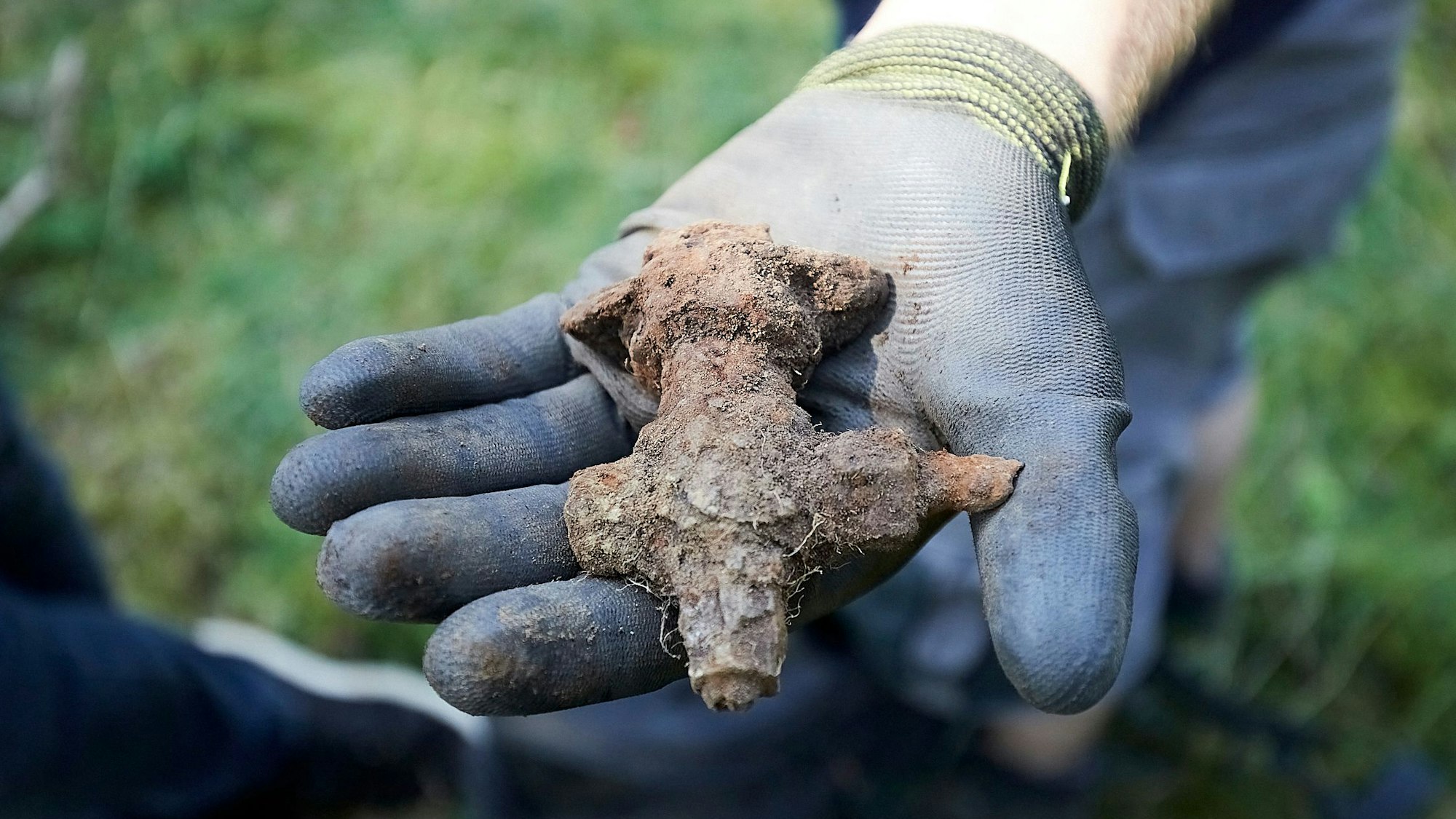 Die linke Hand eines Mannes steckt in einem blauen Arbeitshandschuh, an dem ein wenig Erde haftet. Er zeigt ein verdrecktes und verrostetes Teil einer im Zweiten Weltkrieg über der Eifel abgestürzten V1-Bombe.