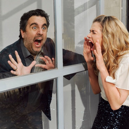 Anke Engelke und Bastian Pastewka befinden sich auf je einer Seite eines Fensters und mimen Panik.