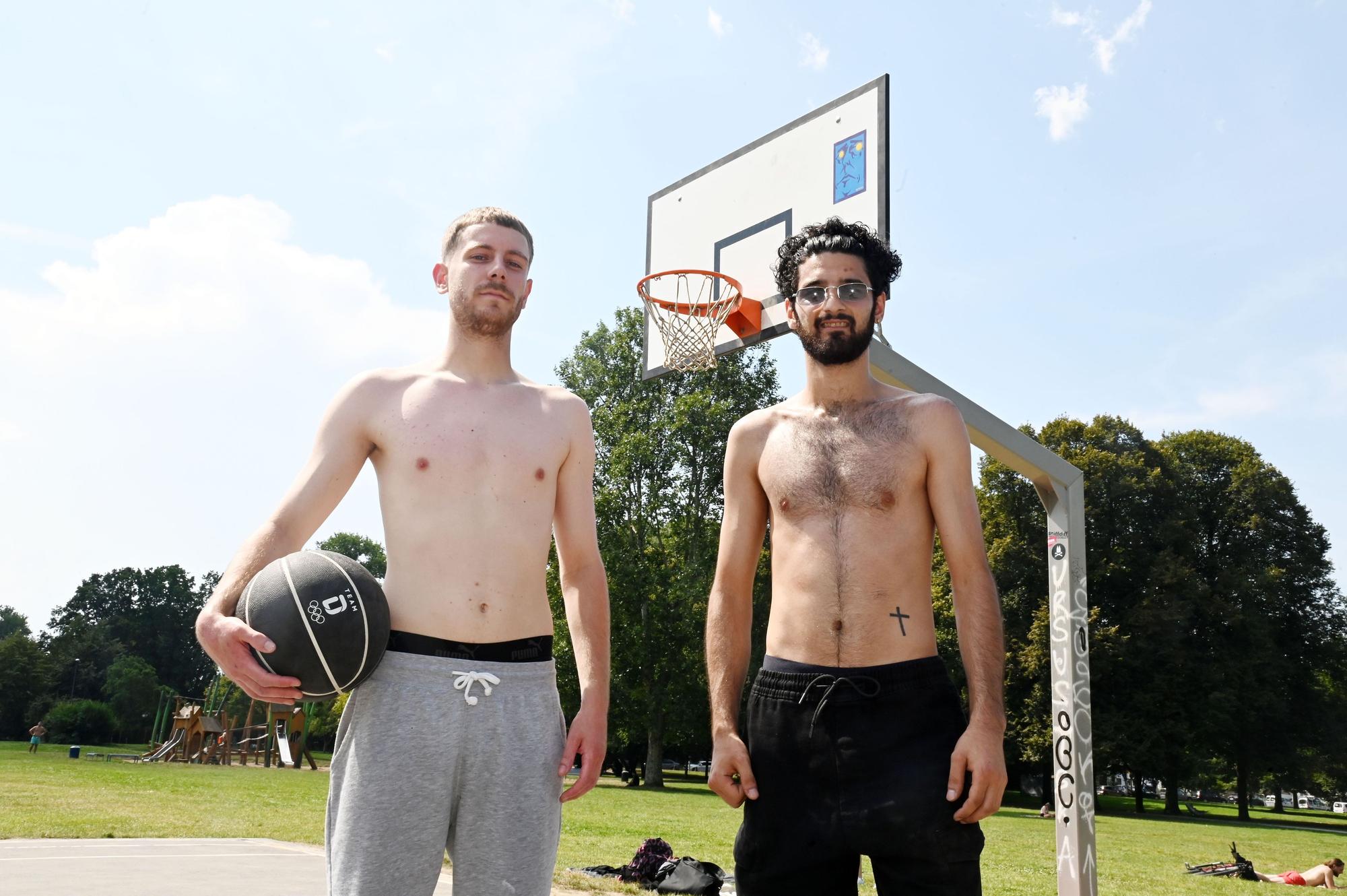 Kevin und Tolga tragen keine Shirts; sie haben einen schwarzen Basketball dabei und lächeln in die Kamera.