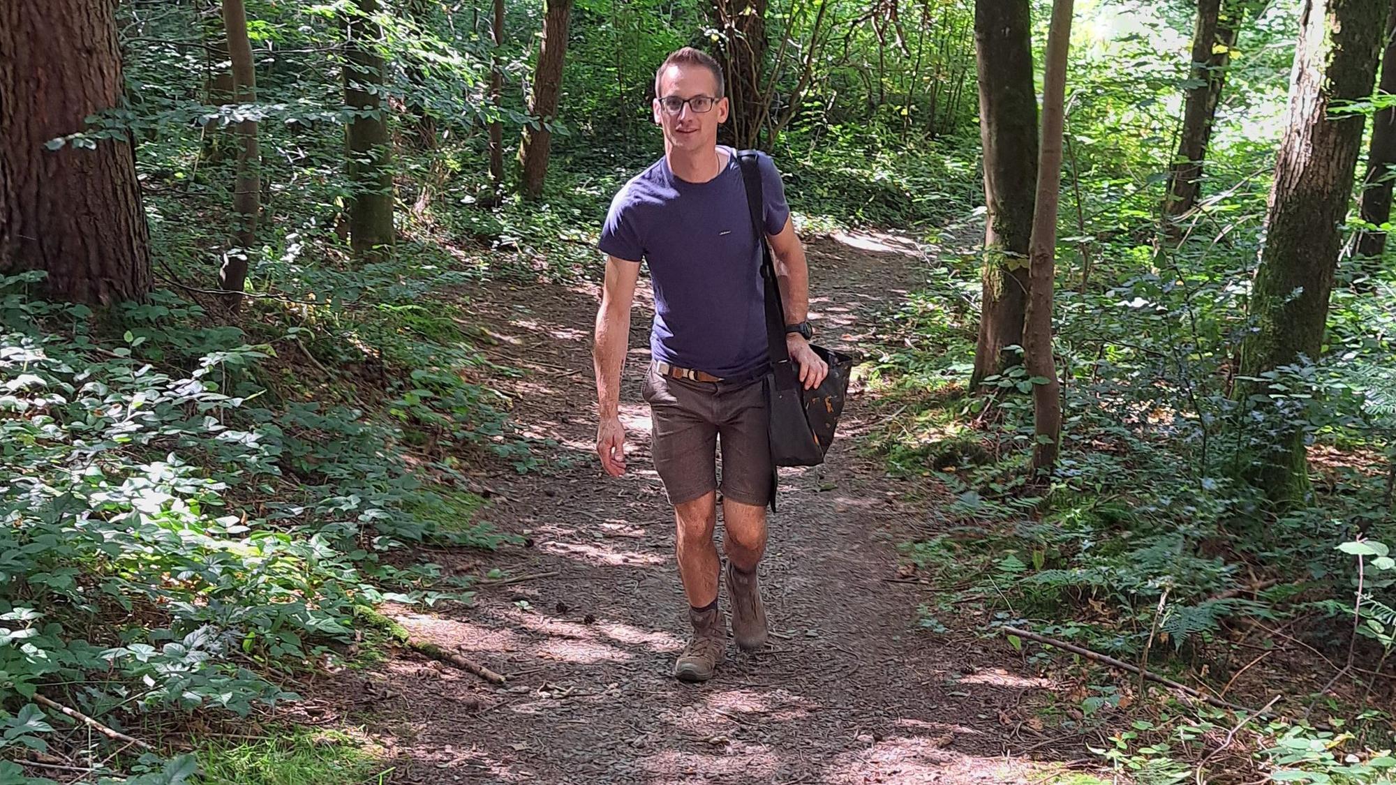 Wegepate Timo Stein geht mit einer Umhängetasche einen Weg hinauf.