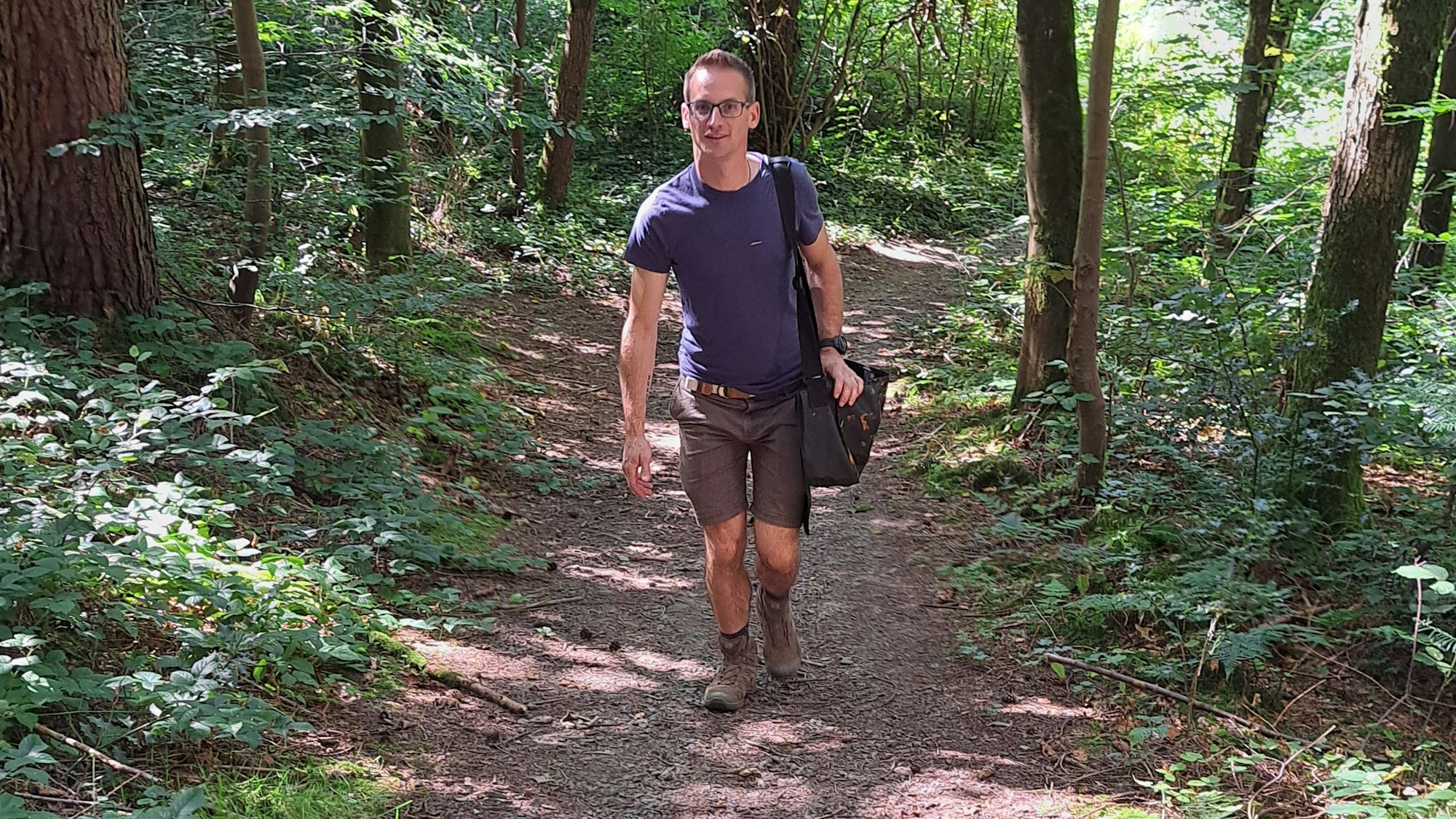 Wegepate Timo Stein geht mit einer Umhängetasche einen Weg hinauf.