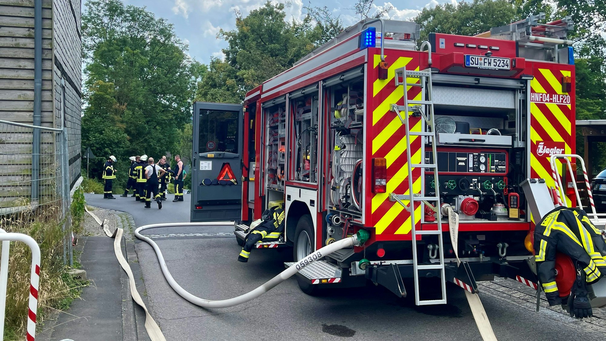 Ein Einsatzfahrzeug und viele Feuerwehrleute stehen auf einer Straße, Schläuche sind ausgerollt.