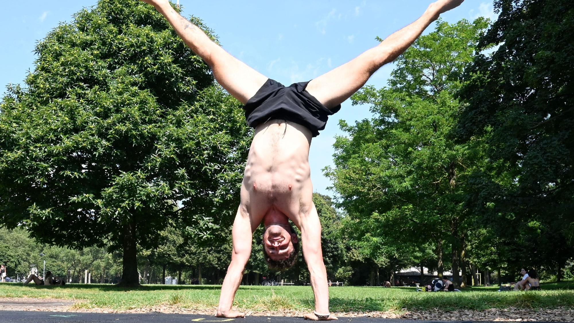 Raphael macht einen Handstand im Kölner Grüngürtel. Hinter ihm sind Bäume zu sehen.