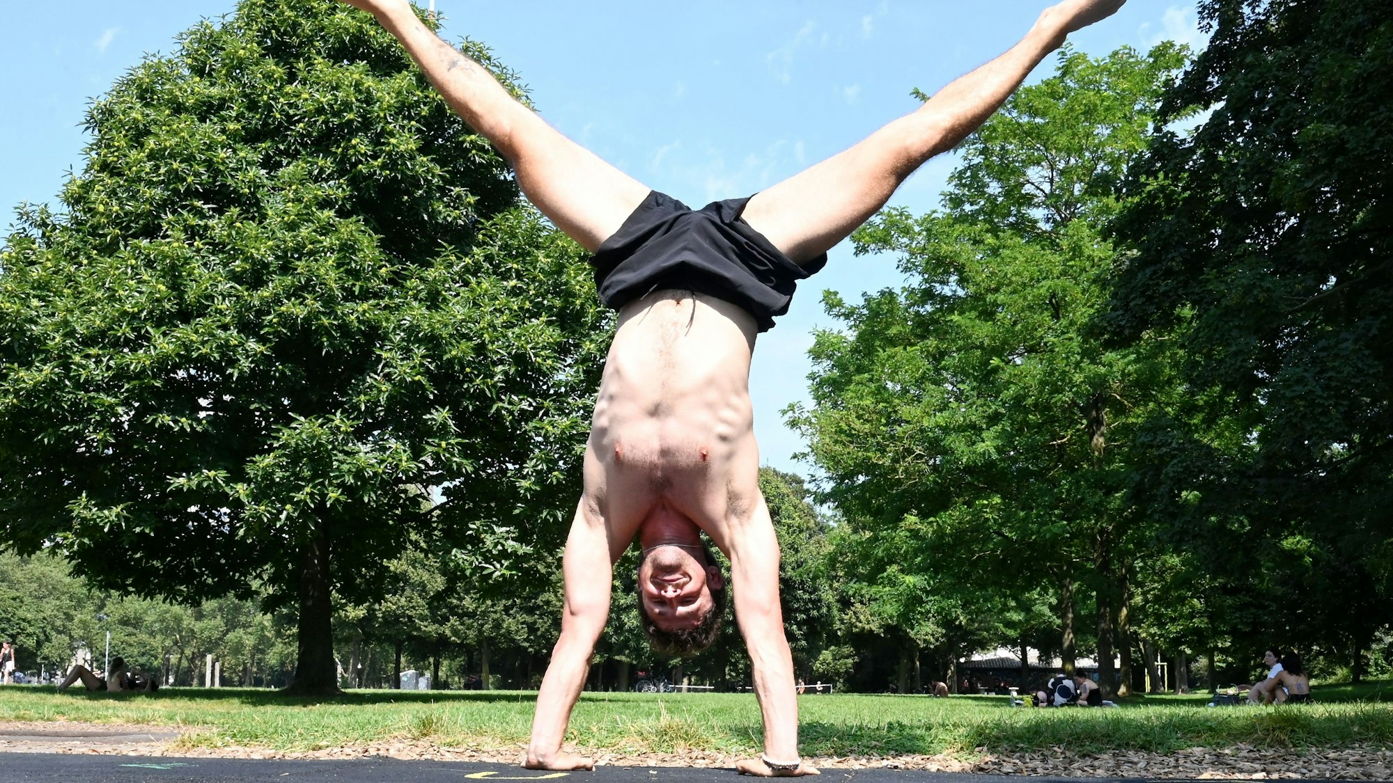Raphael macht einen Handstand im Kölner Grüngürtel. Hinter ihm sind Bäume zu sehen.