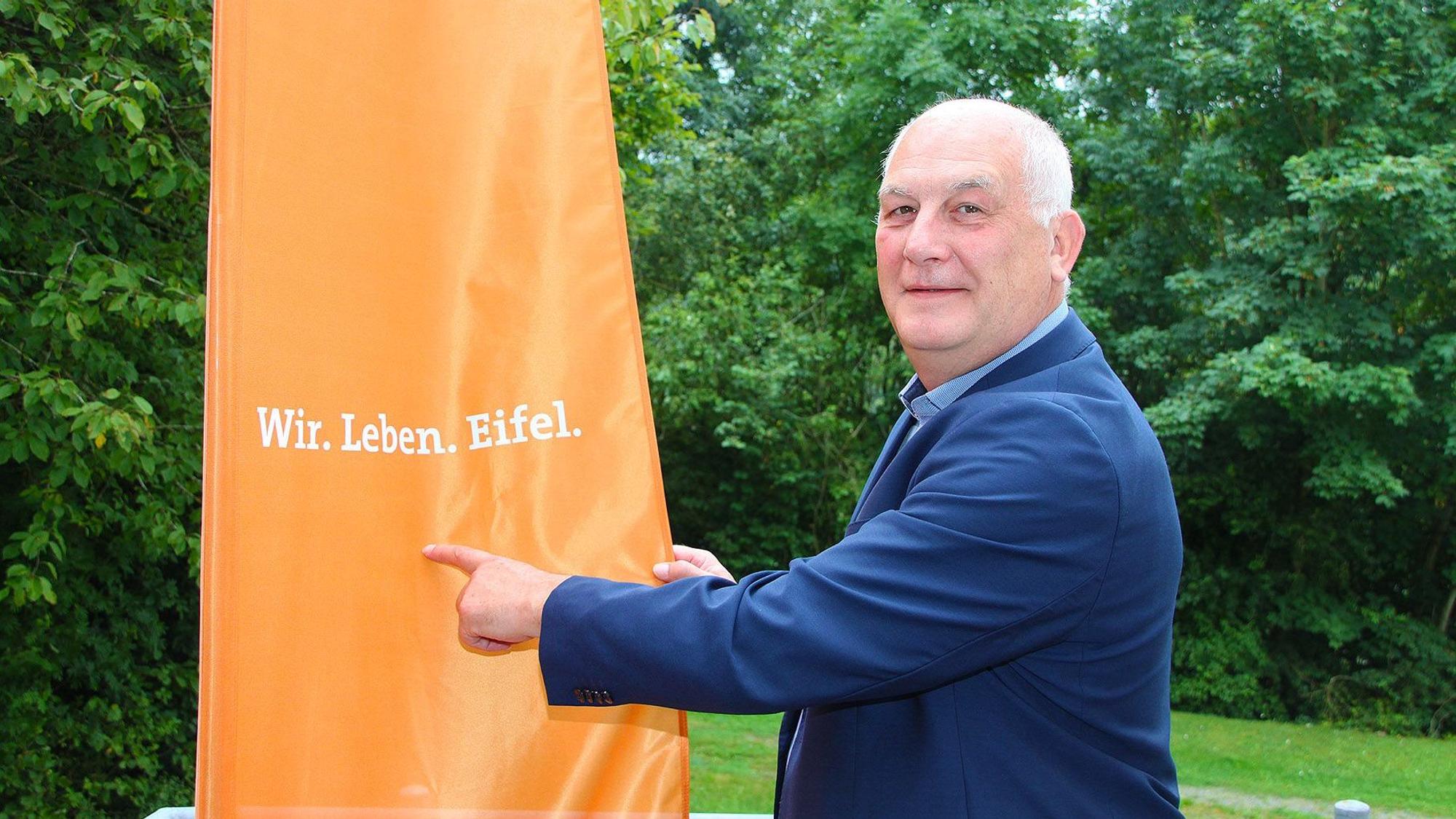 Klaus Schäfer zeigt auf den Slogan „Wir. Leben. Eifel“.