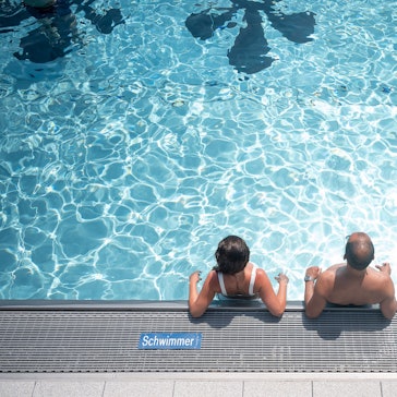Zwei Badegäste stehen am Rand eines Schwimmbeckens und sind aus der Vogelperspektive zu sehen.