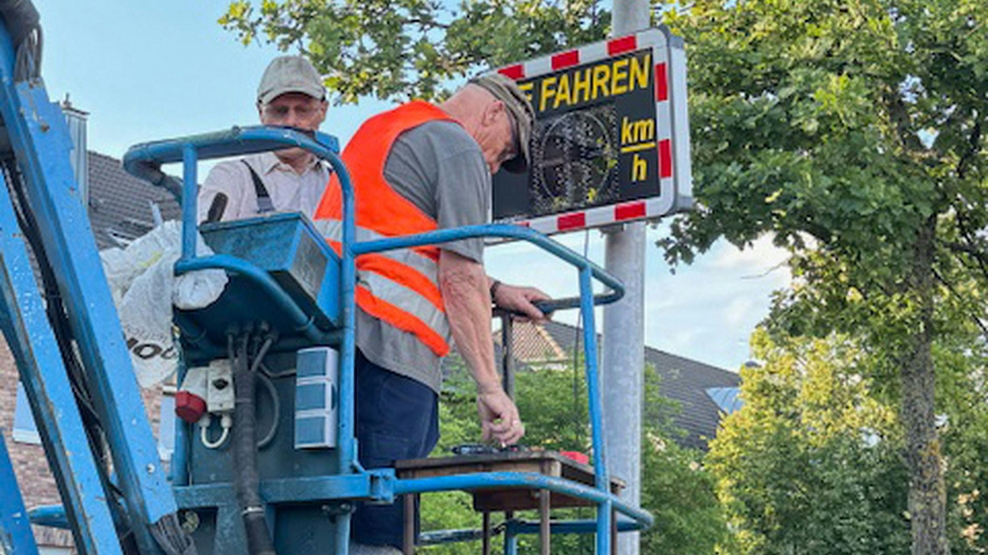 Zwei Männer stehen in Euskirchen-Flamersheim im Korb eines Steigwagens und bringen ein Display an einem Mast an, durch das den Autofahrern die Geschwindigkeit angezeigt wird.