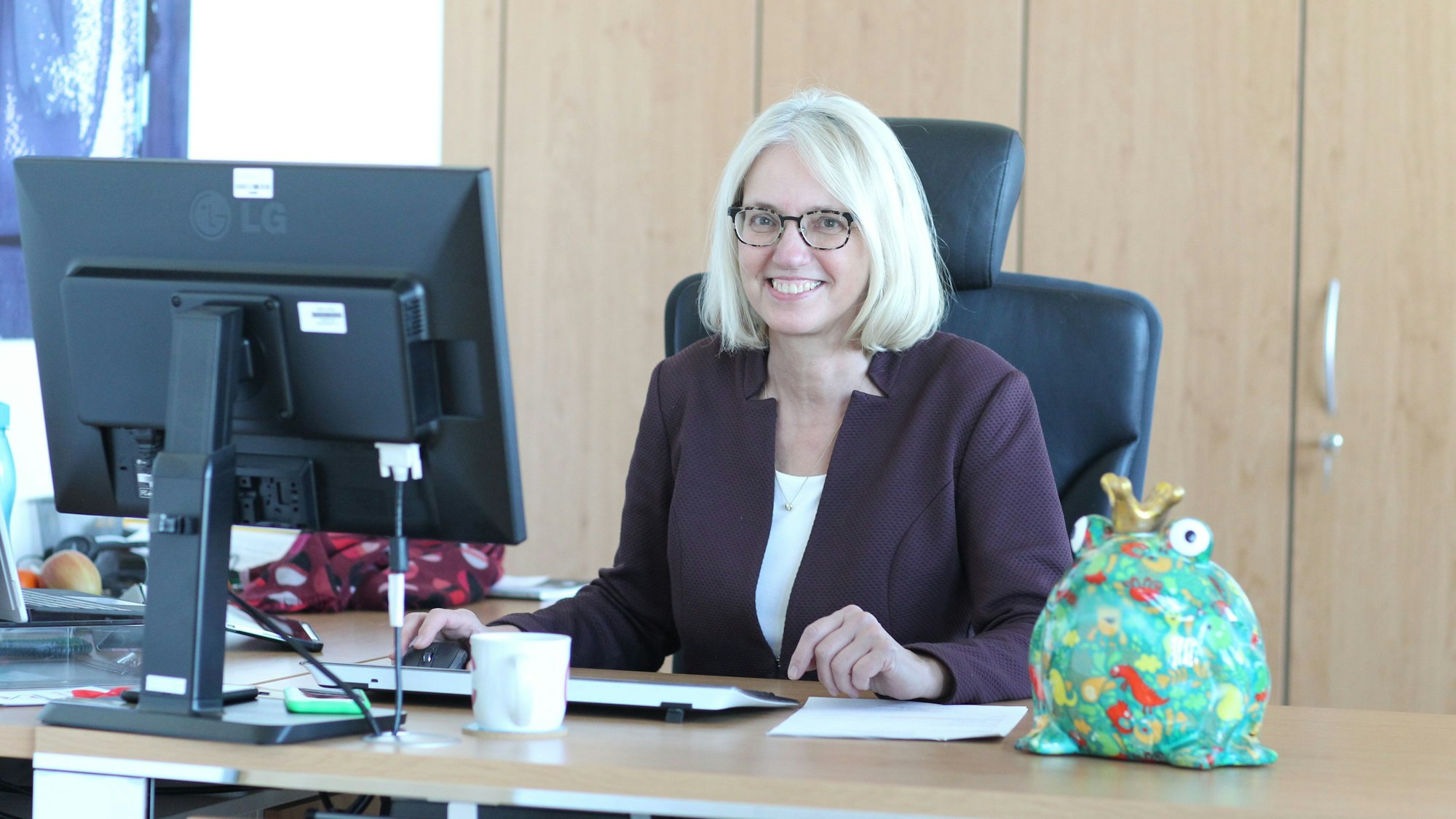 Eie Frau an einem Schreibtisch, darauf ein grüner Froschkönig