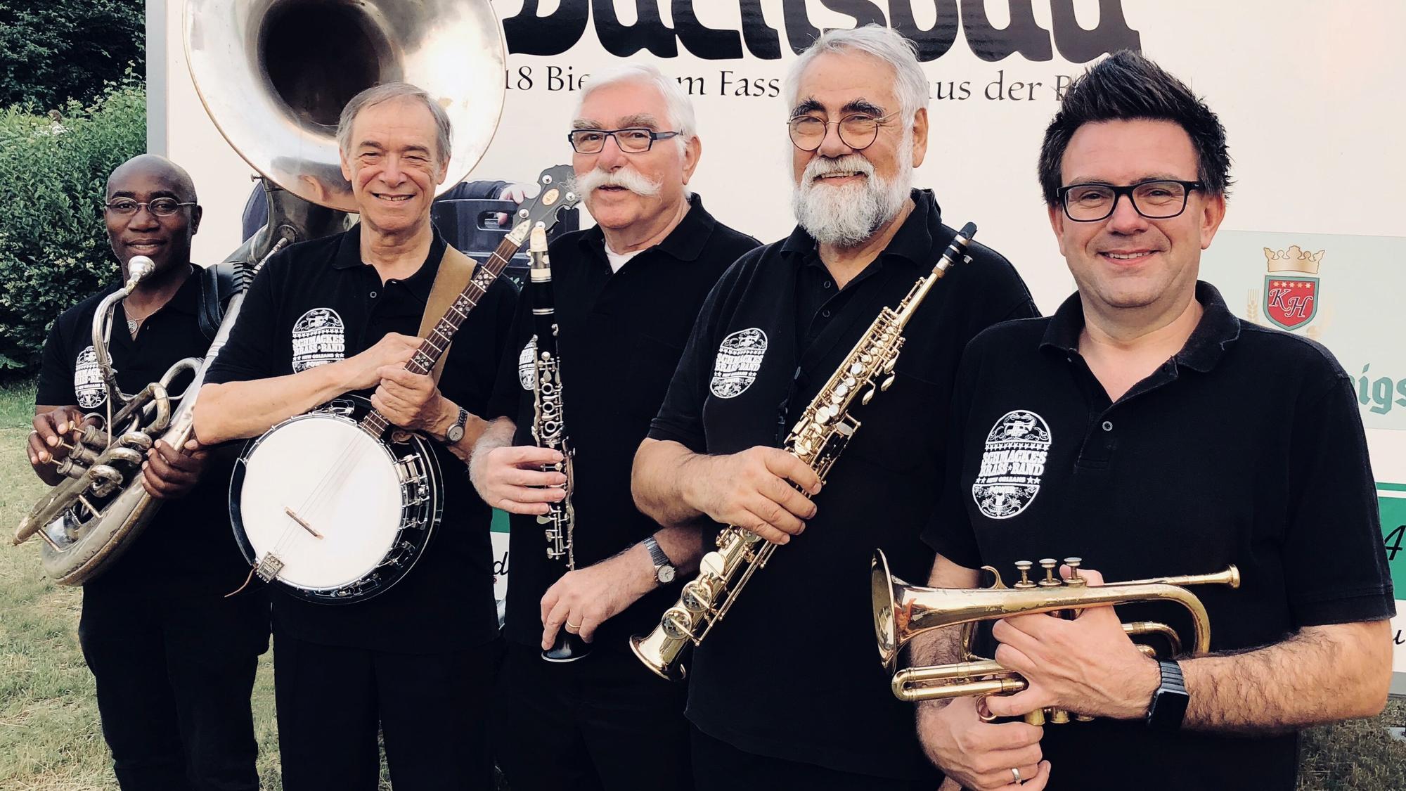 Fünf Musiker, bekleidet mit schwarzen T-Shirts, lächeln in die Kamera.