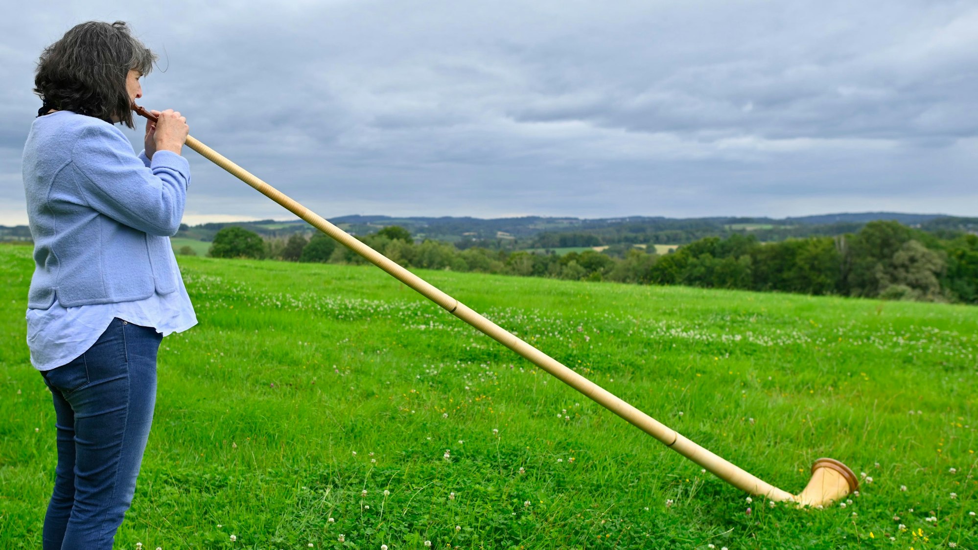 Eine Frau spielt auf einer Wiese Alphorn.
