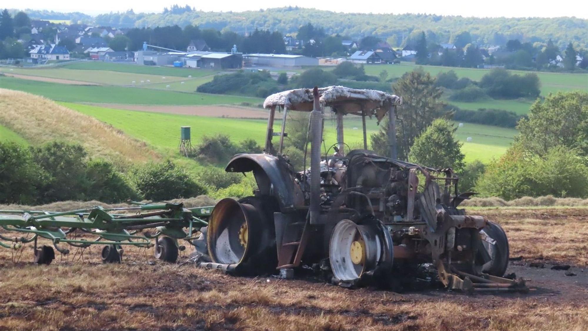 Ein Traktor steht völlig ausgebrannt auf einer Wiese, ein Heuwender ist angeschirrt.