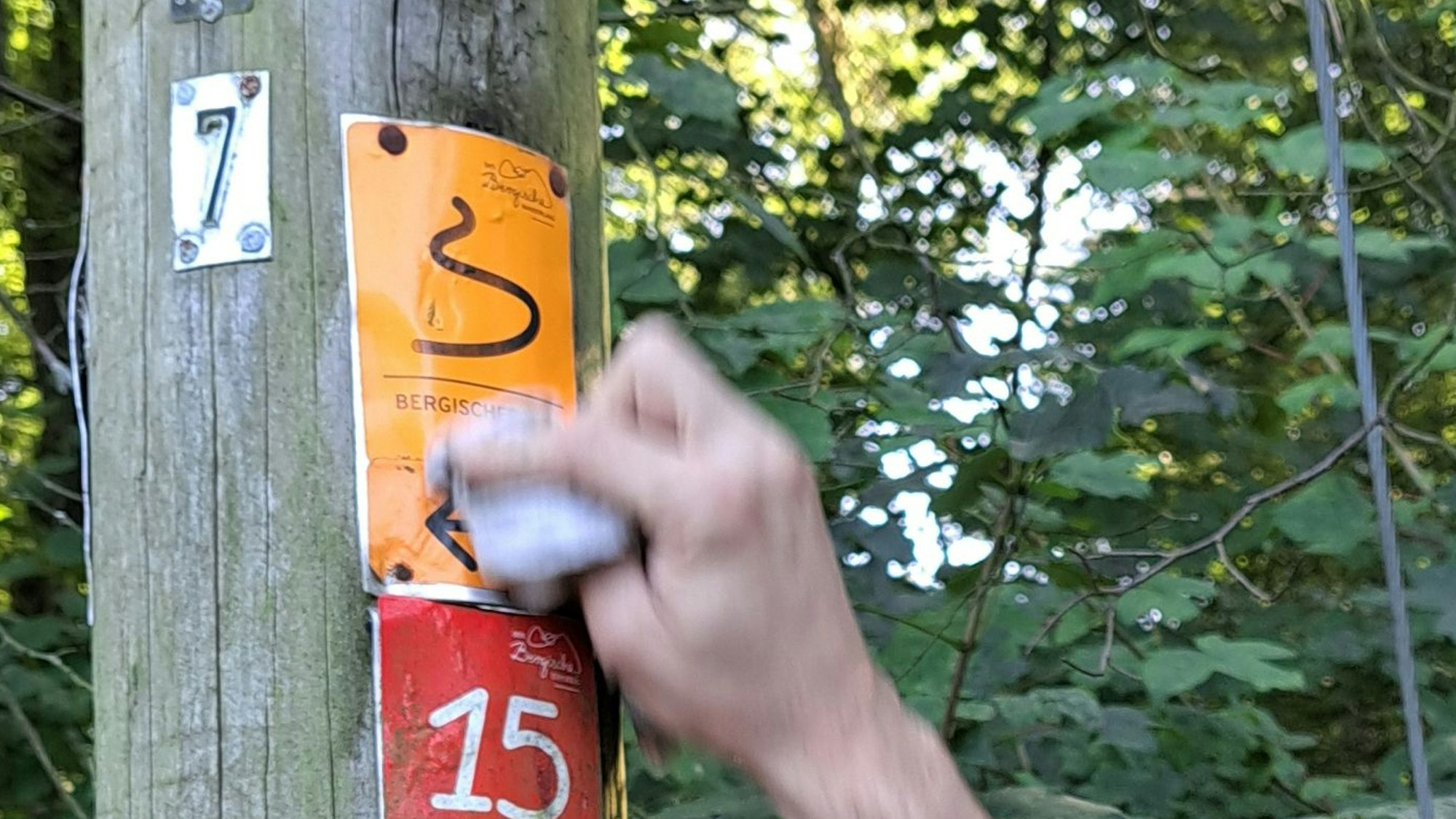 Eine Hand wischt eine Wegemarkierung des Bergischen Wegs ab.