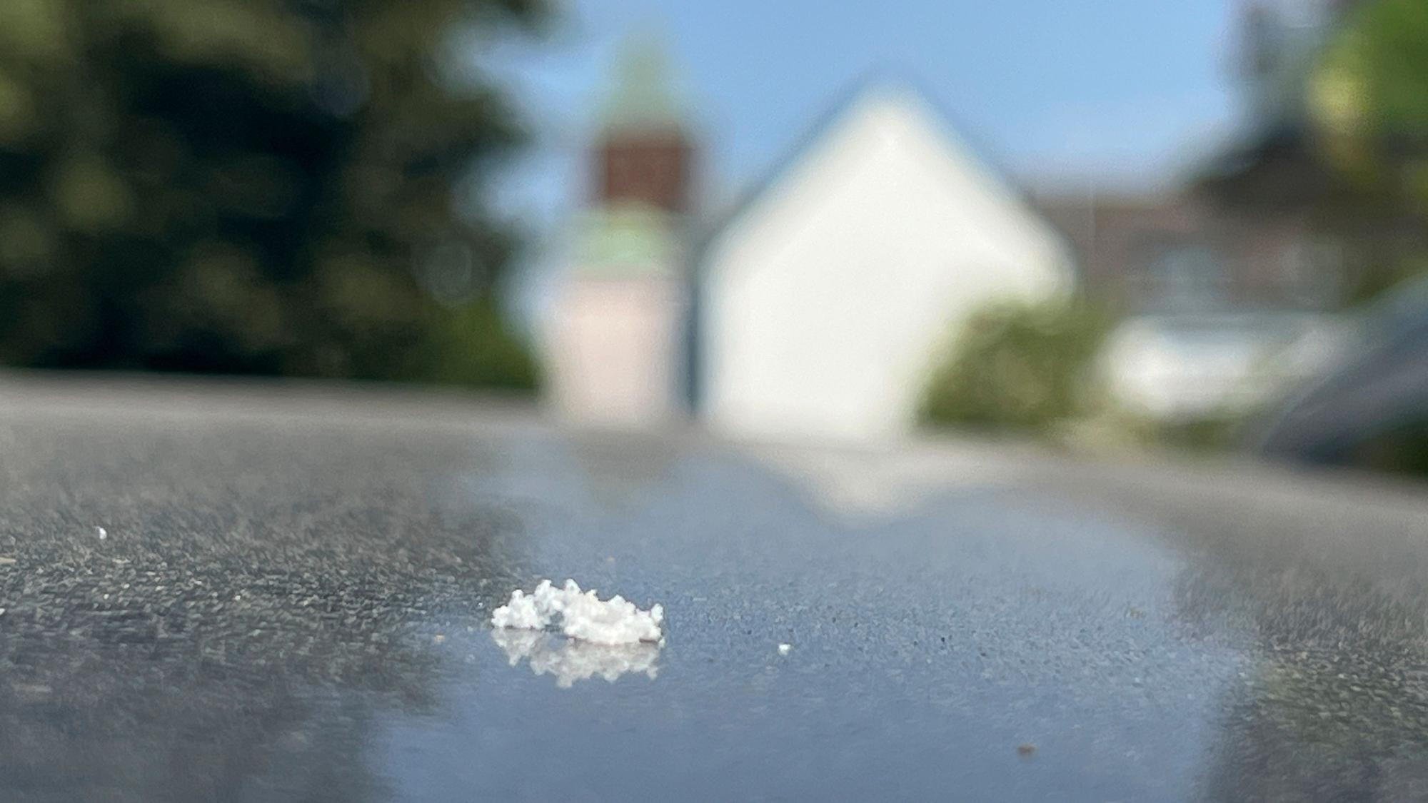 Weiße Flöckchen auf einem Auto in Bürrig, im Hintergrund die Kirche, sie stellen sich als kleinste Styrol-Teilchen heraus. Foto: Ralf Krieger