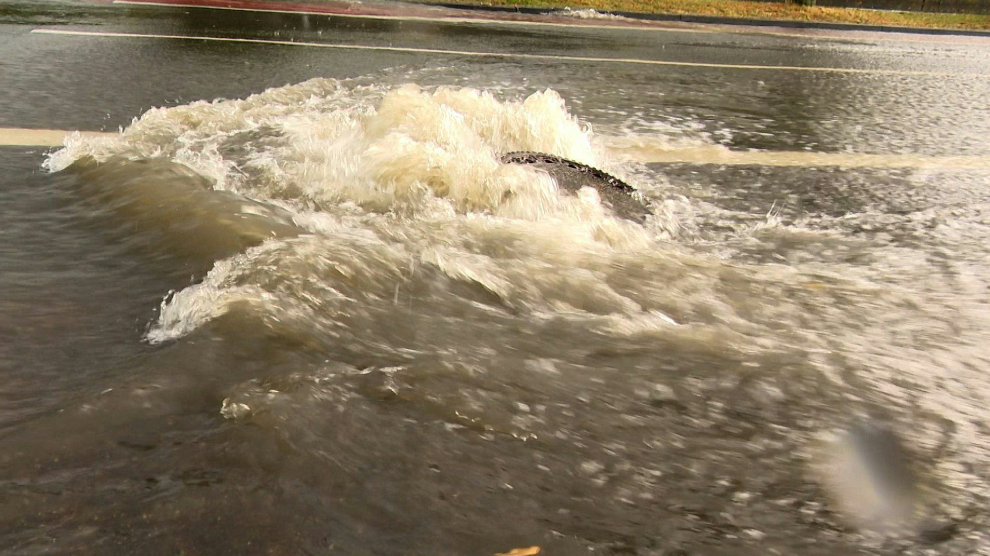 Auf dem Foto ist zu sehen, wie ein Gullideckel von den Wassermassen nach oben gedrückt wird.