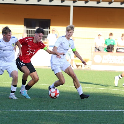 Der Kapitän der JSG Erft 01 hat den Ball und wehrt zwei Dürener Gegenspieler ab.