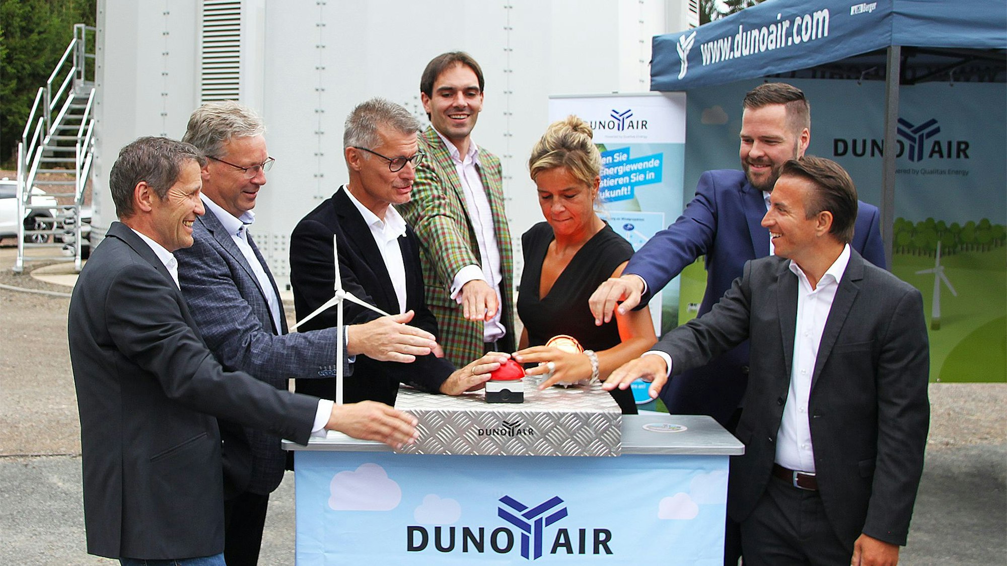 Rechts und links von NRW-Ministerin Mona Neubaur stehen einige Männer. Sie alle drücken auf einen roten Buzzer, um eine Windkraftanlage in Betrieb zu nehmen.