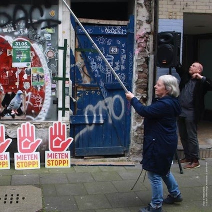 Die Fassade des leerstehenden "Taubenhauses" ist zu sehen. Davor Mahnschilder mit der Aufschrift "Mieten stoppen".
