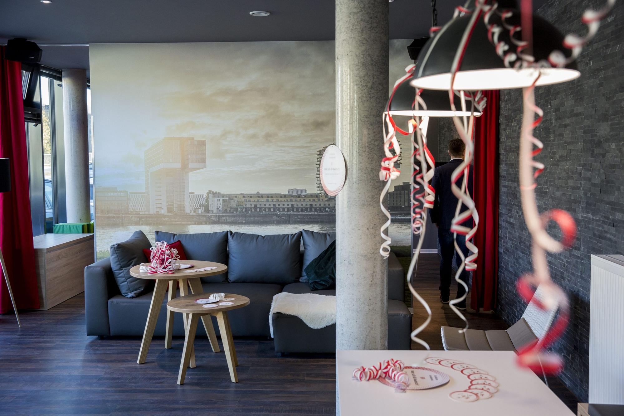 Eröffnung eines Hauses mit Mikroapartments der Firma iLive.
Urban living Köln. Ein Wohnzimmer mit Beistelltischen ist zu sehen. Über zwei Leuchten sind mit Luftschlangen dekoriert.