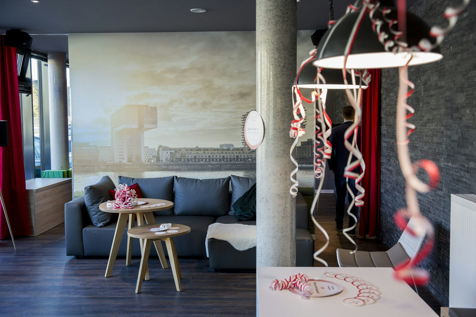 Eröffnung eines Hauses mit Mikroapartments der Firma iLive.
Urban living Köln. Ein Wohnzimmer mit Beistelltischen ist zu sehen. Über zwei Leuchten sind mit Luftschlangen dekoriert.