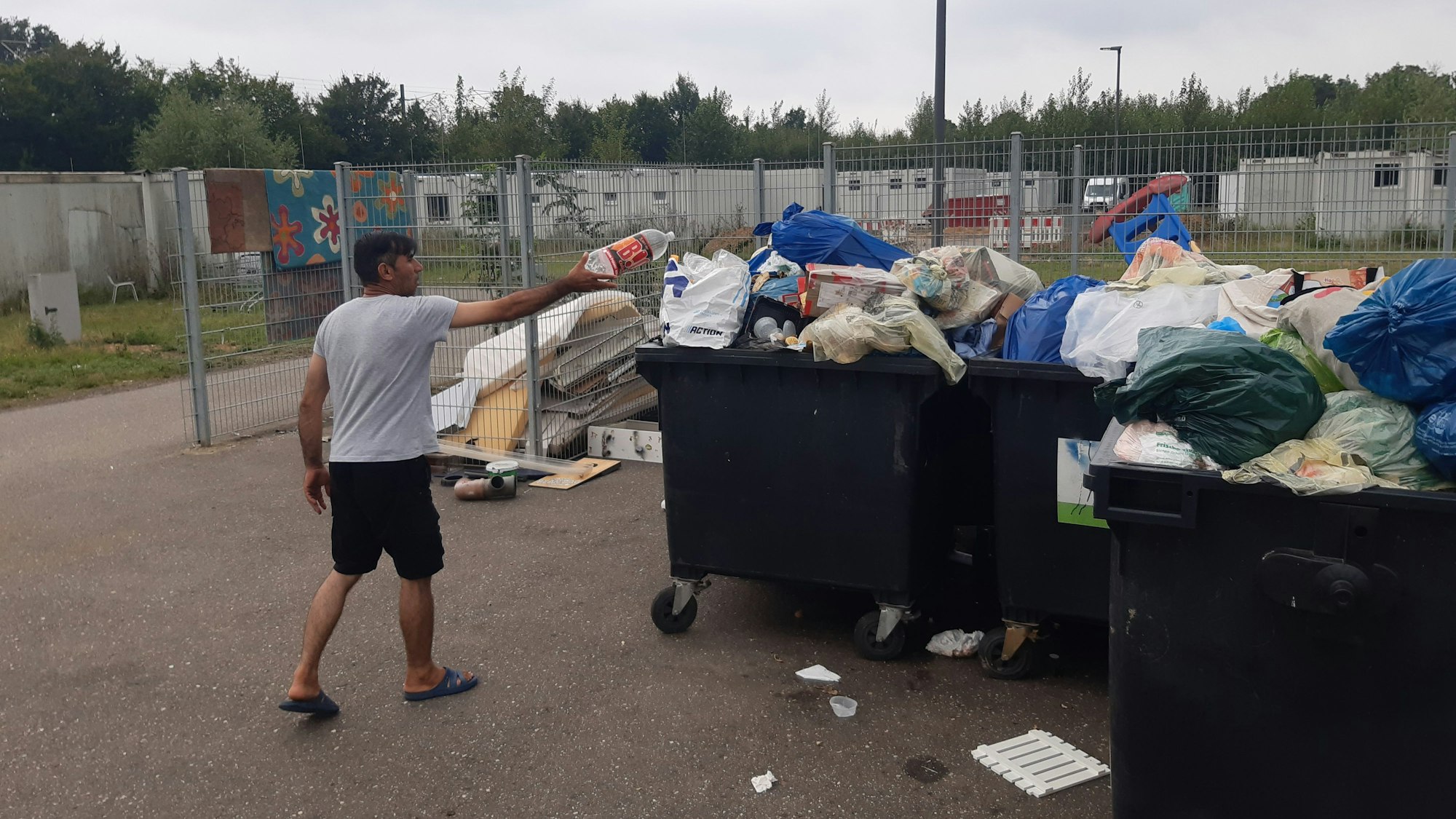 Ein Mann versucht, eine Plastikflasche in übervollen Müllcontainern vor einer Flüchtlingsunterkunft zu entsorgen.