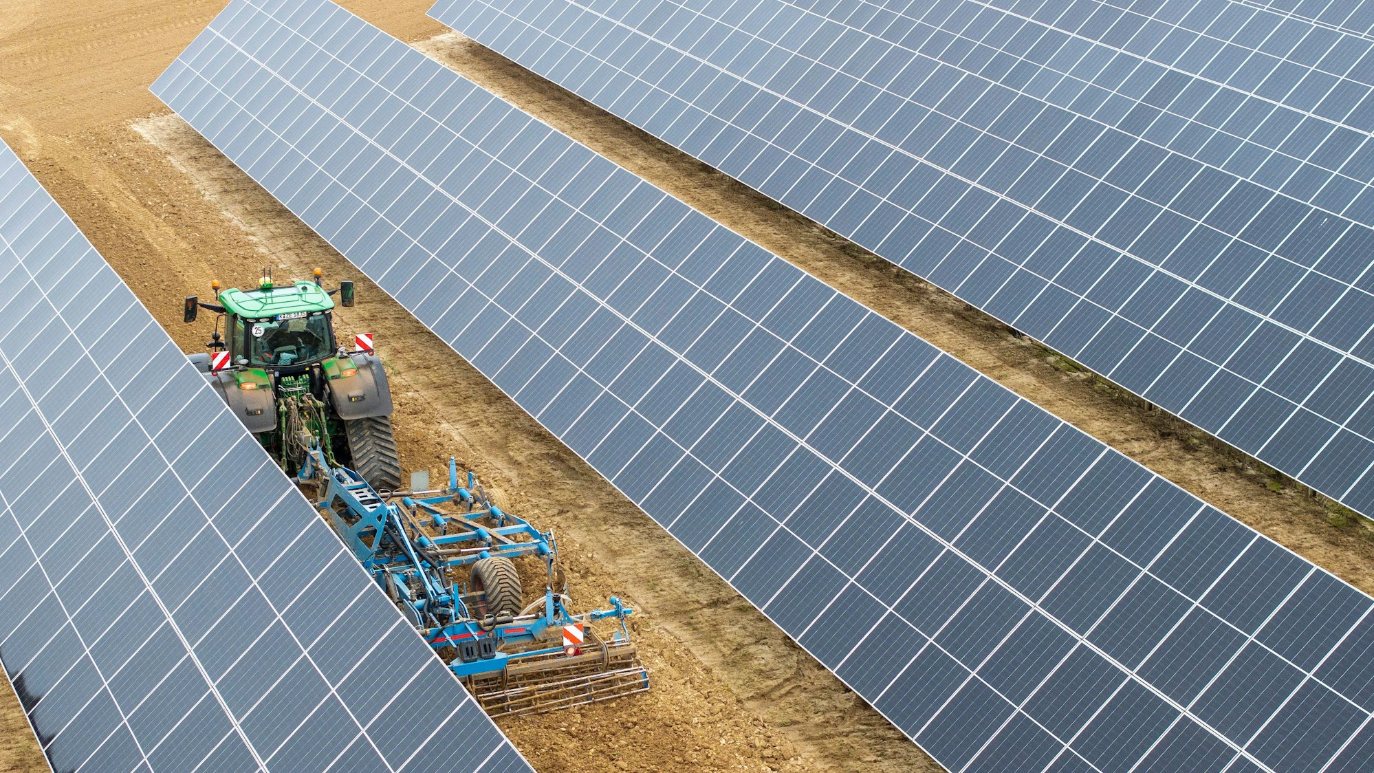 Schräg stehende Solramodule stehen auf brauner Ackerfläche.