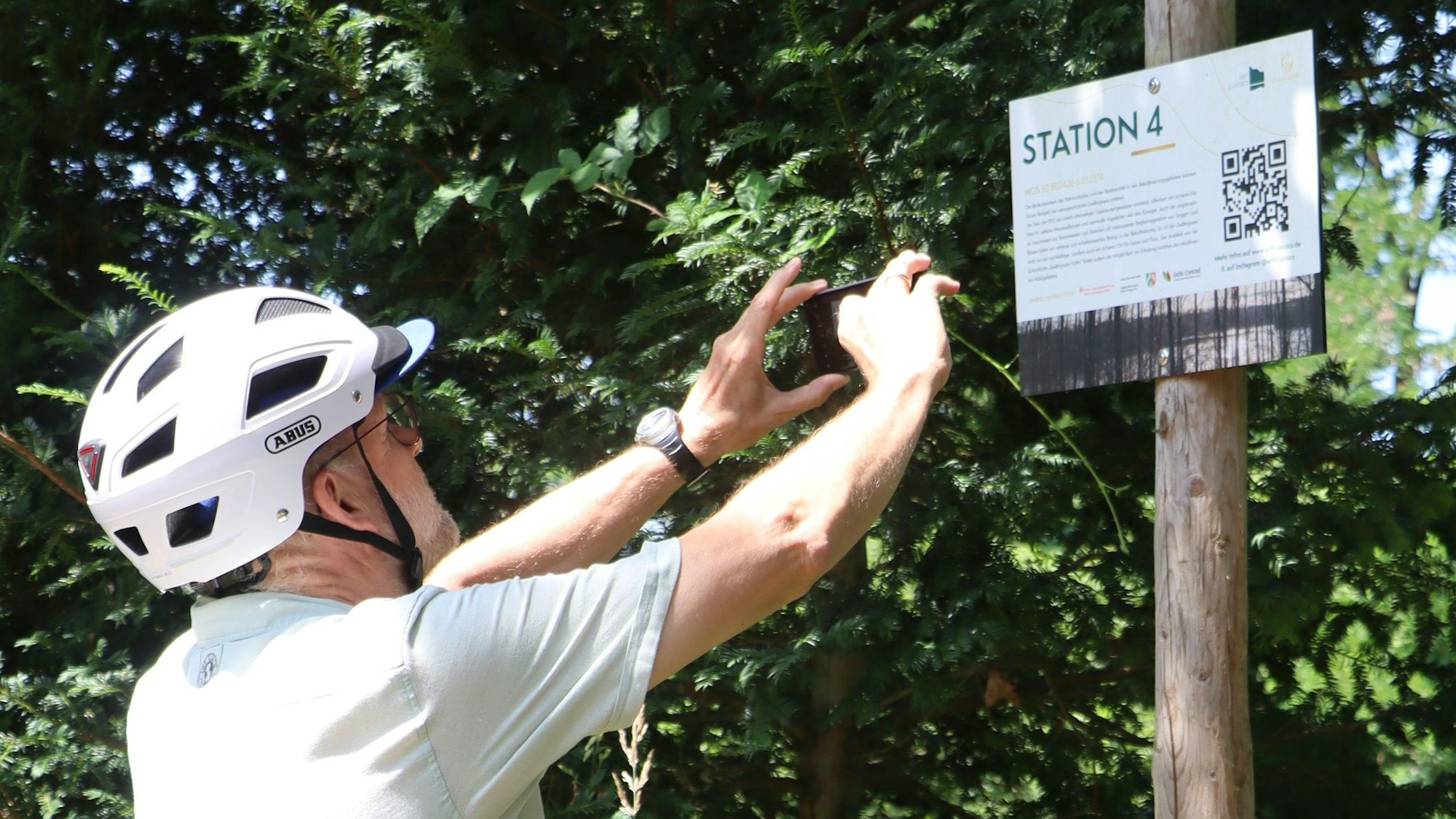 Das Bild zeigt einen Fahrradfahrer, der mit einem Handy einen QR-Code scannt.