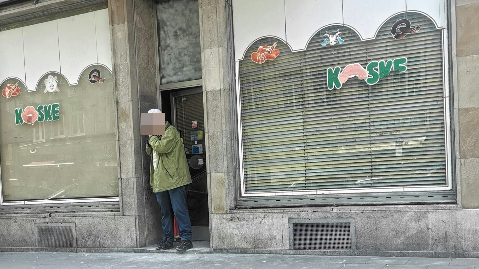 Ein Ladenlokal mit heruntergelassenen Jalousien ist zu sehen. Ein Mann steht im Eingang.