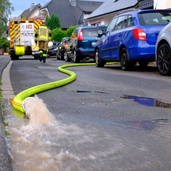 Wasser sprudelt aus einem gelben Feuerwehrschlauch: Helfer der Freiwilligen Feuerwehr pumpen nach einem Starkregenereignis am 13.8.24 Keller in der Rehgasse in Kommern aus.