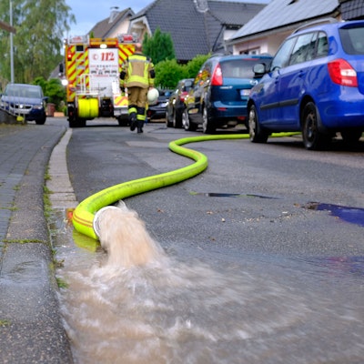 Wasser sprudelt aus einem gelben Feuerwehrschlauch: Helfer der Freiwilligen Feuerwehr pumpen nach einem Starkregenereignis am 13.8.24 Keller in der Rehgasse in Kommern aus.