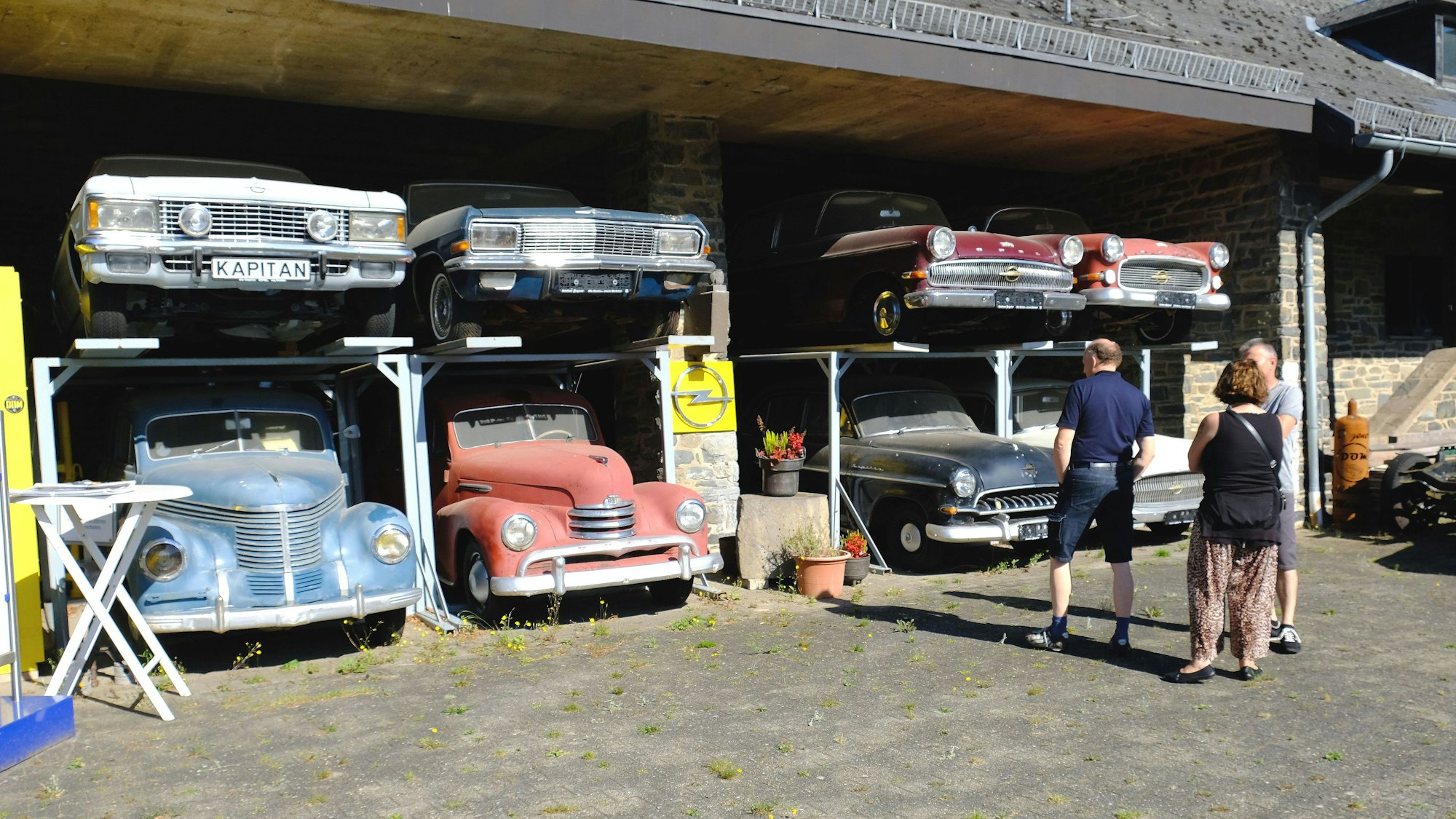 Drei Museumsbesucher stehen vor insgesamt acht Fahrzeugen des Typs Opel Kapitän aus verschiedenen Baujahren.