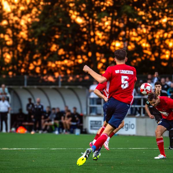 Ein Lommersumer Spieler köpft einen Ball. Im Hintergrund glüht der Himmel orange.