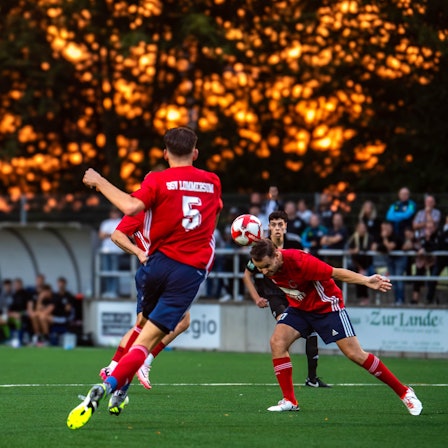 Ein Lommersumer Spieler köpft einen Ball. Im Hintergrund glüht der Himmel orange.