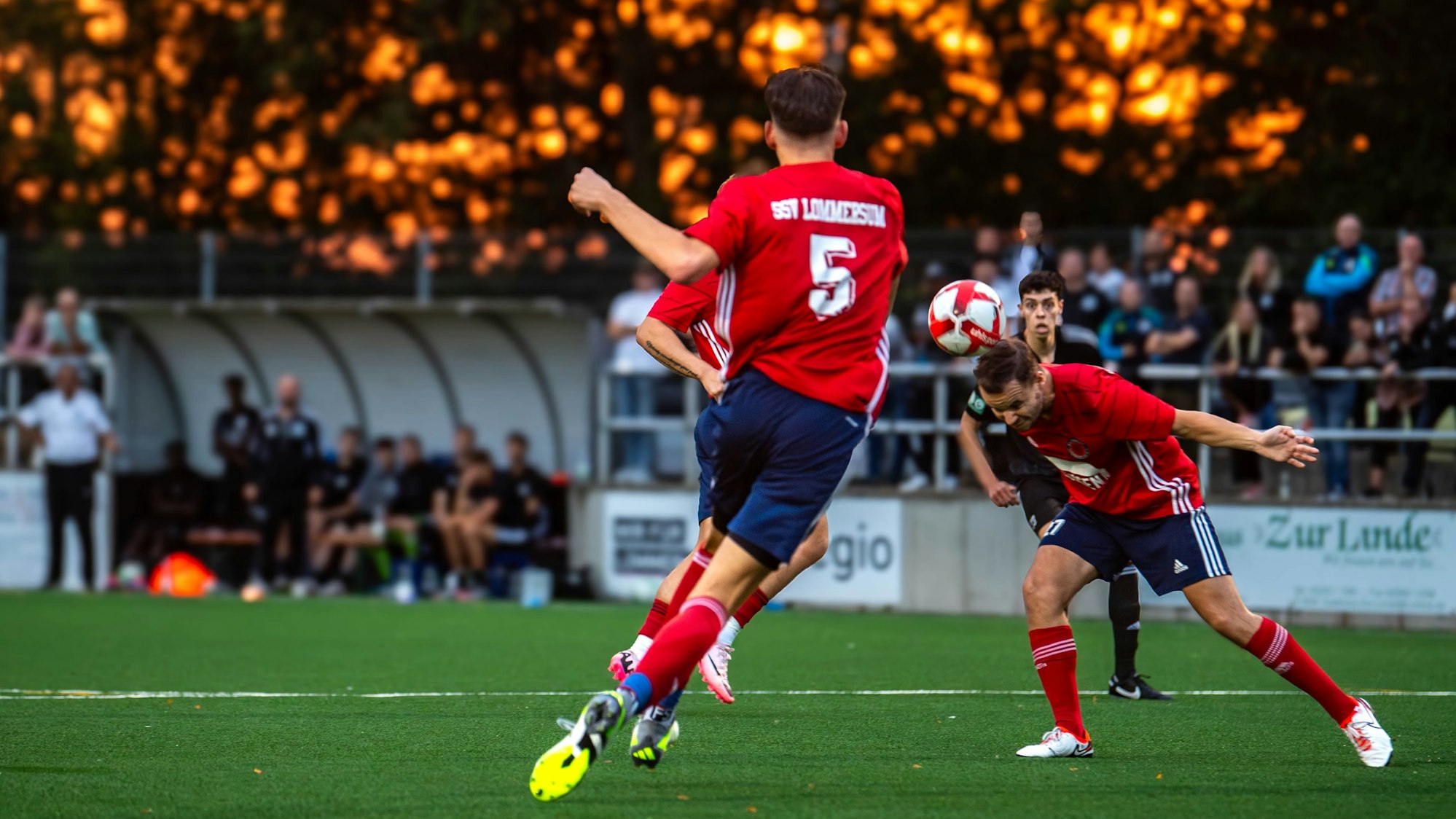 Ein Lommersumer Spieler köpft einen Ball. Im Hintergrund glüht der Himmel orange.