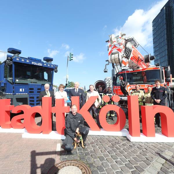 Henriette Reker, Oberbürgermeisterin von Köln, (2.v.l.) und Johannes Hermanns (l), Polizeipräsident stehen im Rheinauhafen mit Behördenvertretern vor dem Schriftzug der Stadt Köln zwischen Einsatzfahrzeugen.