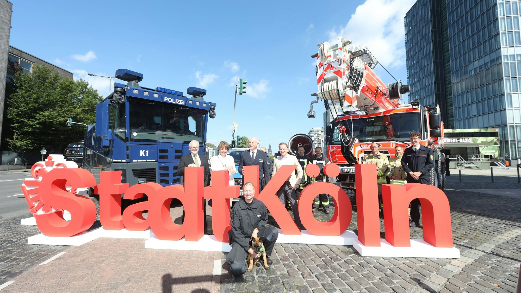 Henriette Reker, Oberbürgermeisterin von Köln, (2.v.l.) und Johannes Hermanns (l), Polizeipräsident stehen im Rheinauhafen mit Behördenvertretern vor dem Schriftzug der Stadt Köln zwischen Einsatzfahrzeugen.