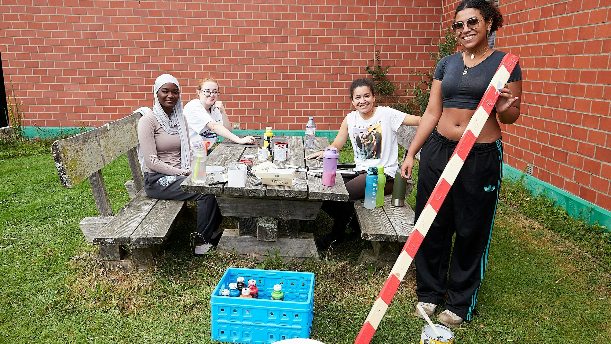 Vier junge Leute sind in einem Garten und basteln vor einer Backsteinwand..