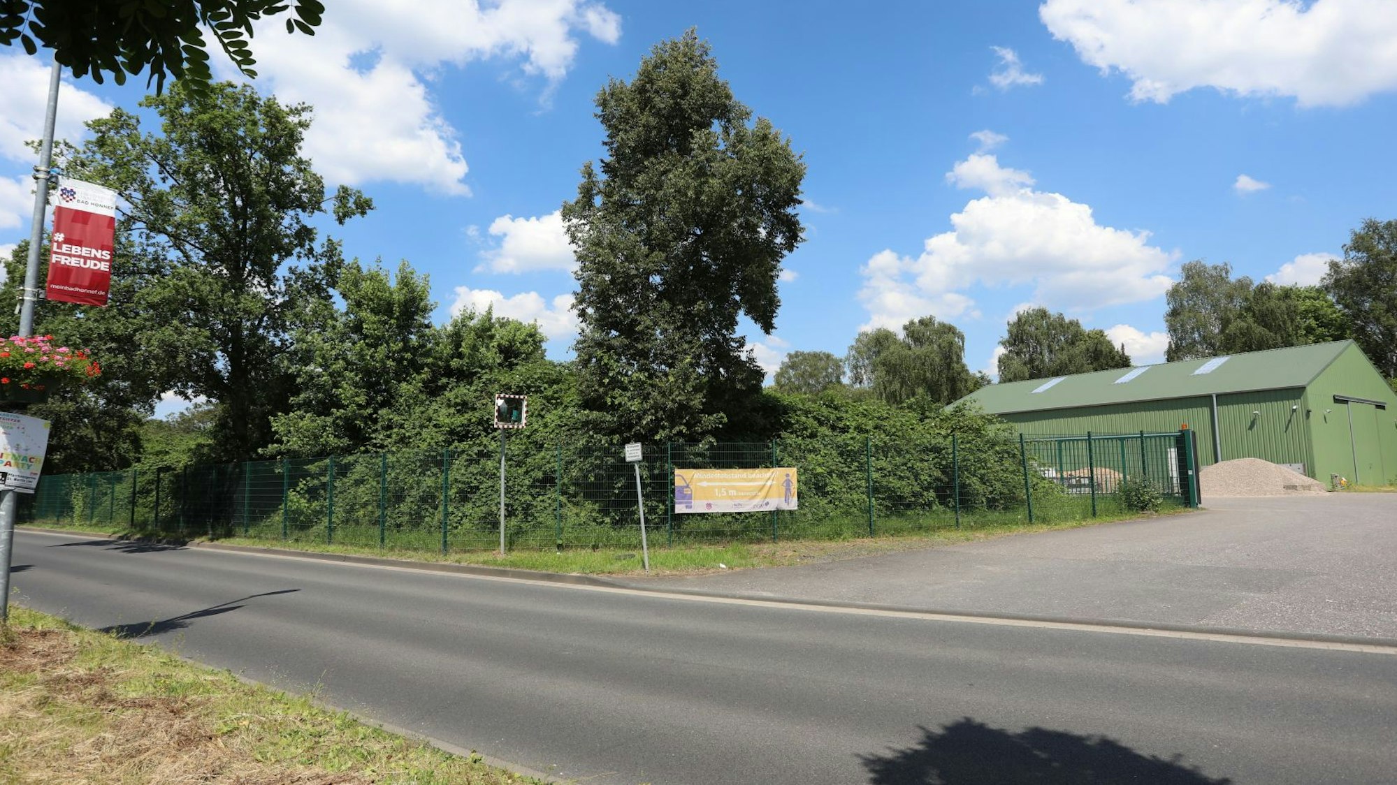 Eine Straße, im Hintergrund eine Zufahrt zu einer grünen Lagerhalle.