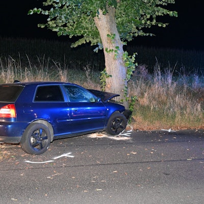 Ein blaues Auto steht kaputt nach einem Unfall an einem Baum. Auf dem Boden Kreidemarkierungen der Polizei.