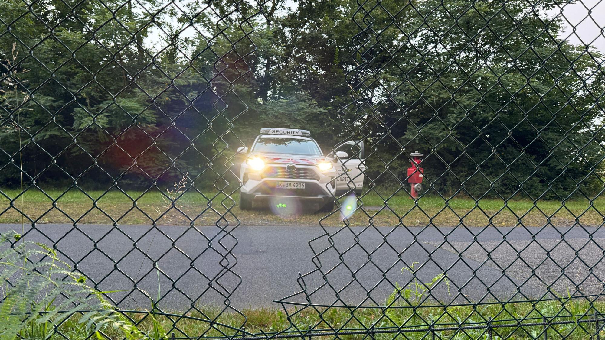 Ein Auto der Flughafensicherheit des Flughafen Köln-Bonn steht hinter dem Zaun des Flughafens. Die Polizei geht davon aus, dass Aktivisten der Klima-Initiative Letzte Generation durch das sichtbare Loch im Zaun auf das Gelände des Flughafens gelangt sind.