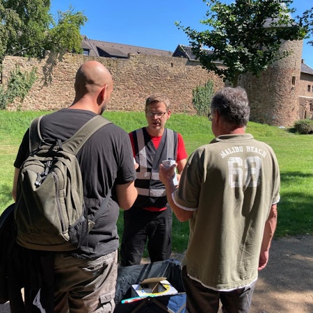Ein Mann reicht zwei Wohnungslosen in einem Park Tetra Paks mit Wasser.