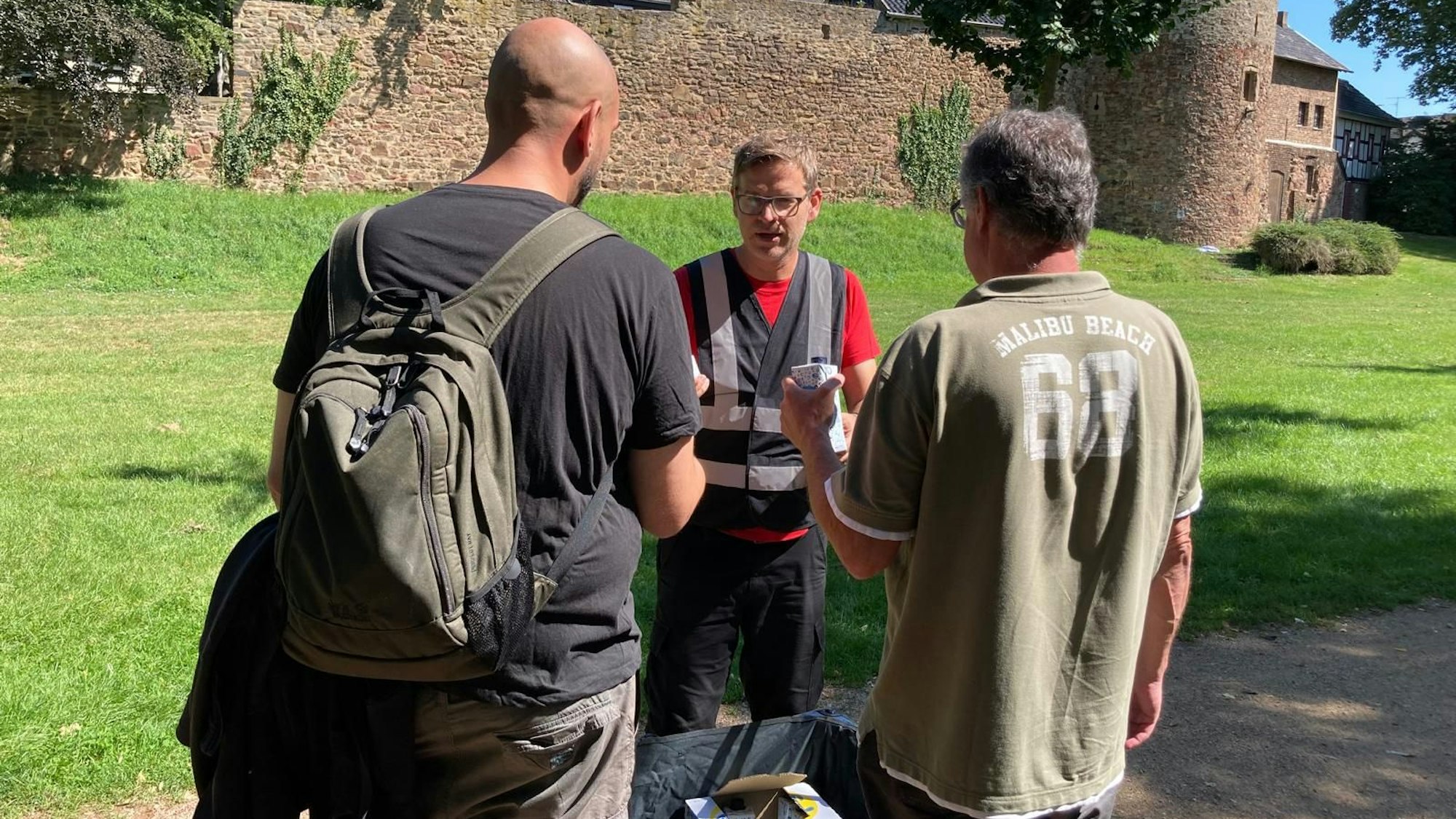 Ein Mann reicht zwei Wohnungslosen in einem Park Tetra Paks mit Wasser.