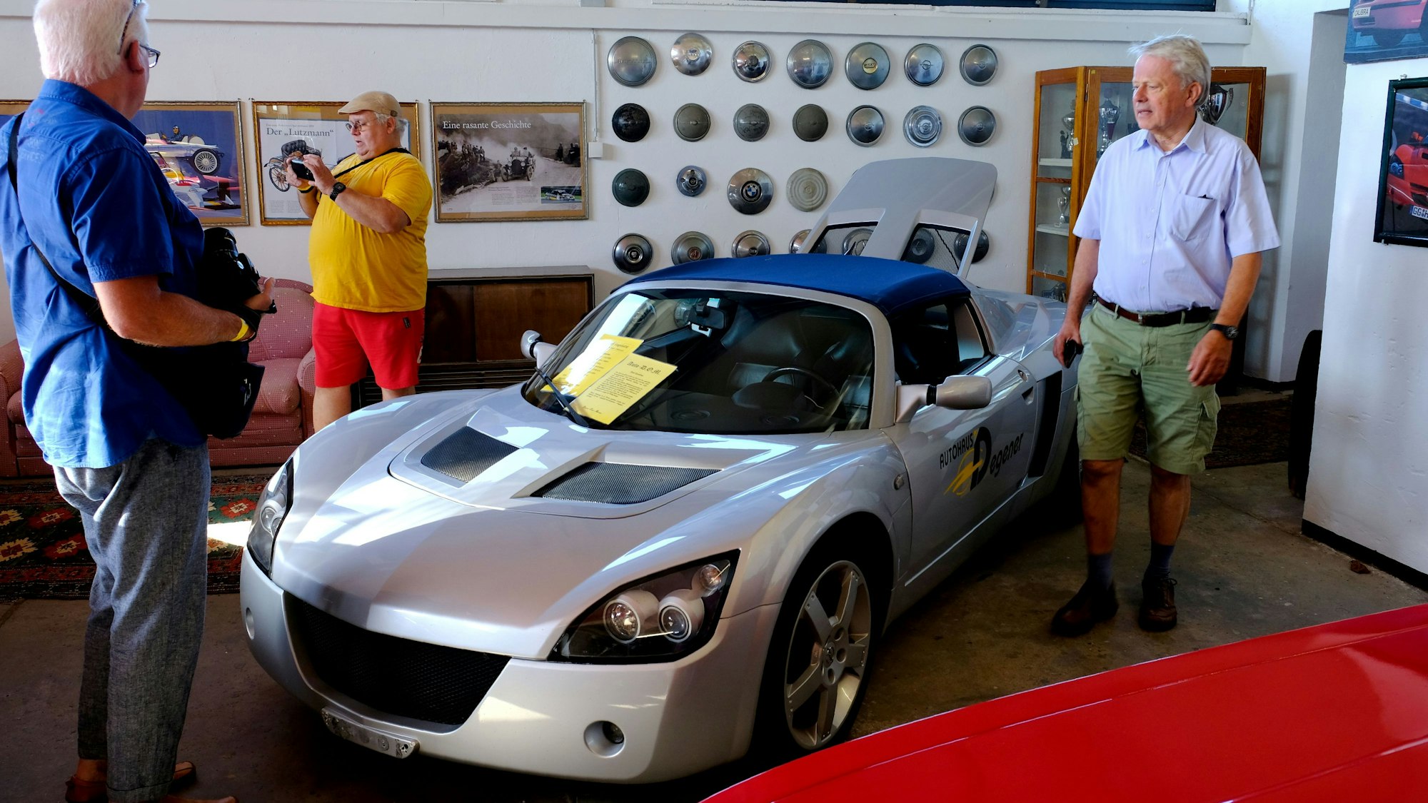 Drei Besucher stehen rund um einen silbernen Opel Speedster.