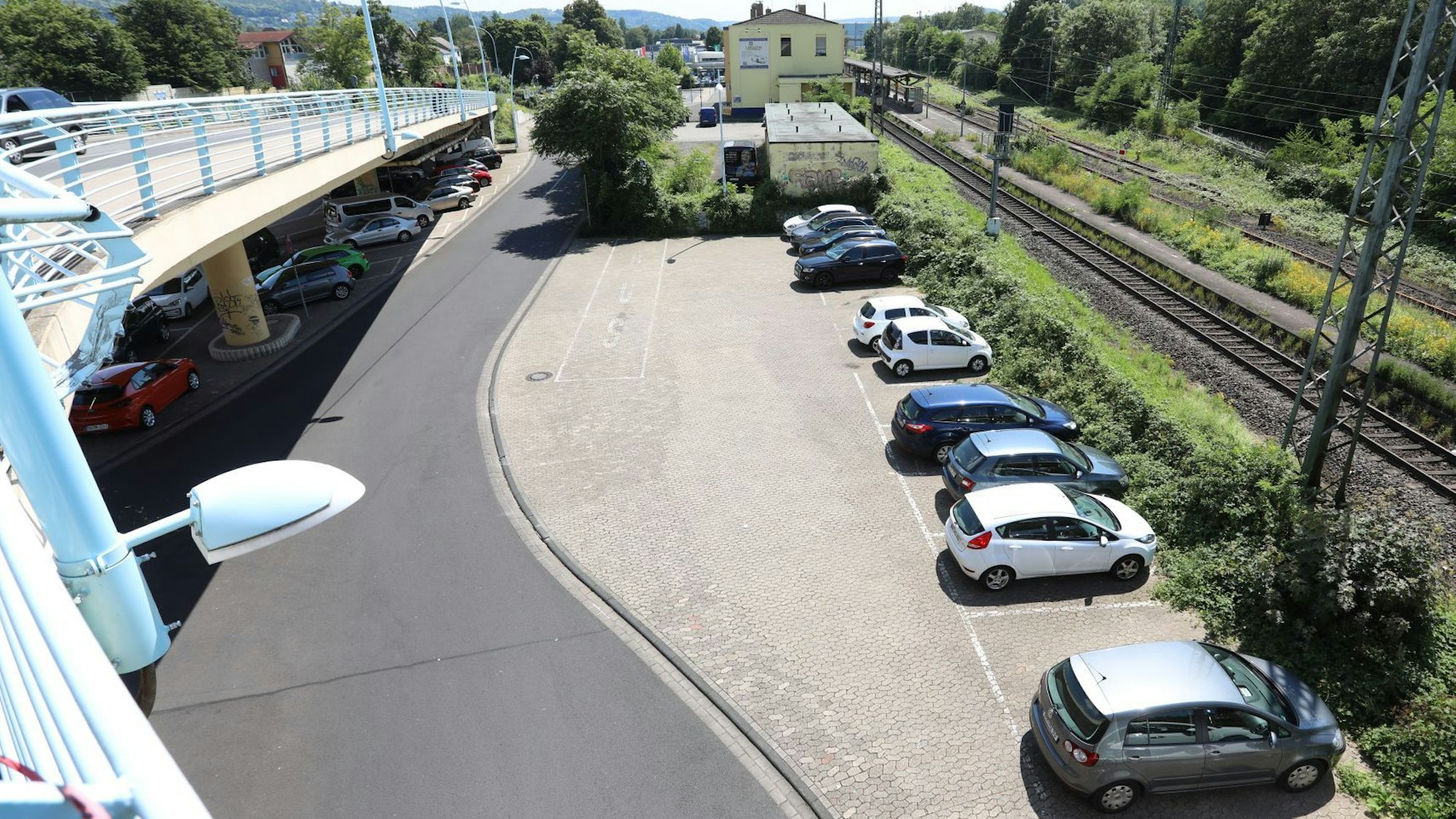 Blick von einer Brücke auf einen Parkplatz, im Hintergrund das Bahnhofsgebäude.