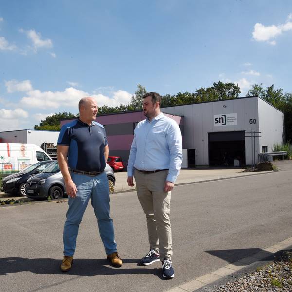 Das Foto zeigt zwei Männer und im Hintergrund zwei Hallen der Firma SN.